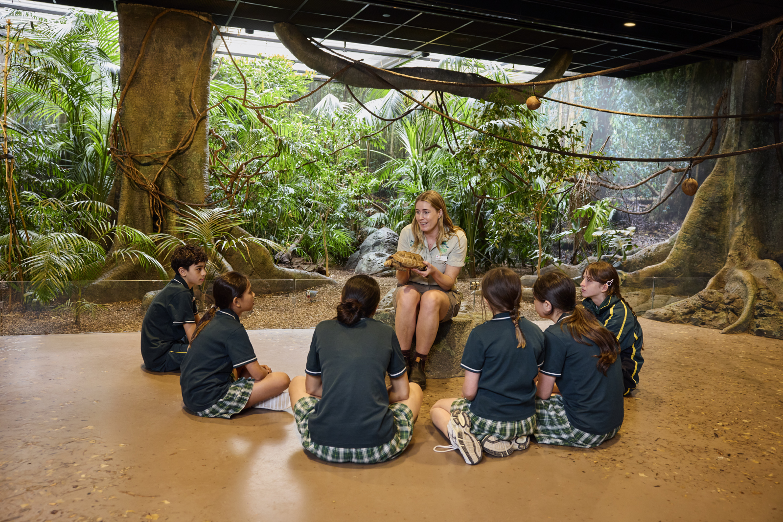 Children in a immersive classroom listening to a teacher with greenery in background.